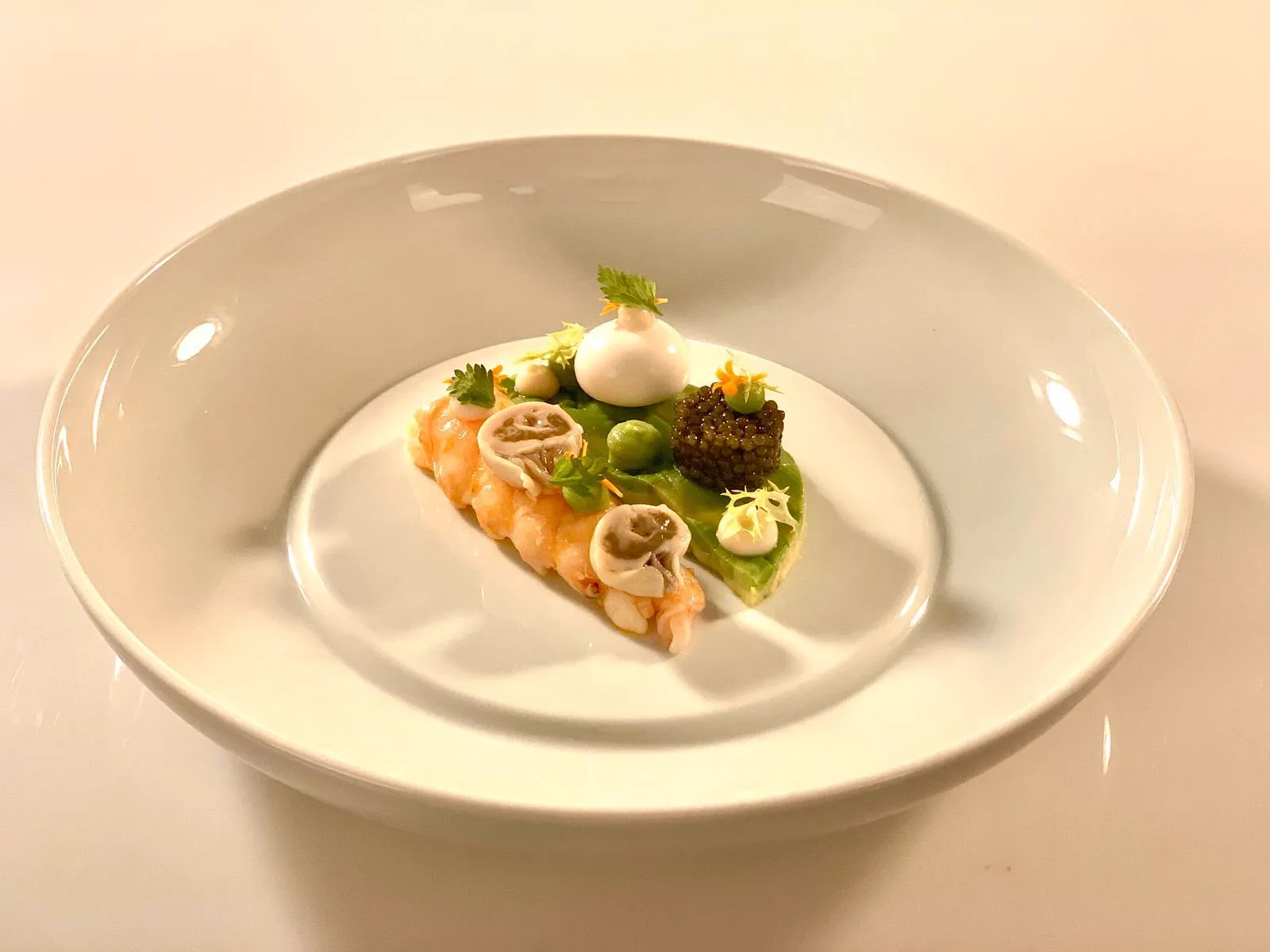 Cola de cigala con caviar imperial, puré verde, crema, hierbas y flores comestibles, emplatada por un chef en un restaurante con estrella Michelin