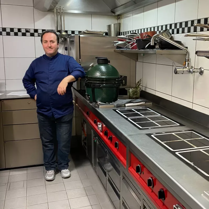 A chef in his restaurant kitchen beside a ceramic kamado grill