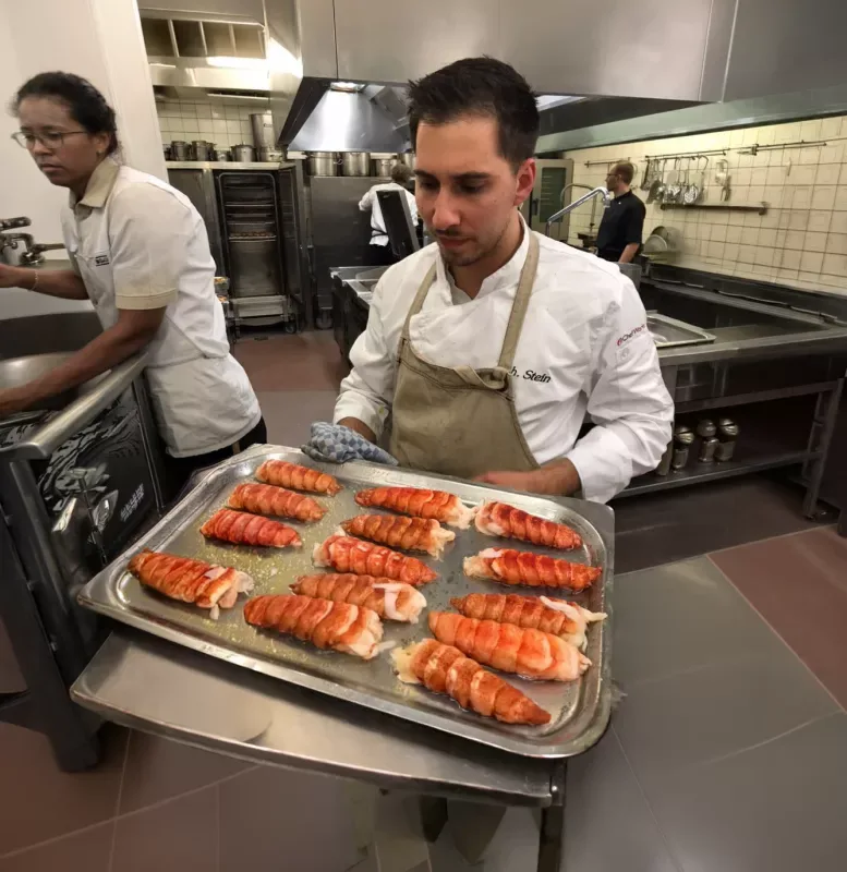 A chef carrying a tray of roasted lobster tails through his restaurant kitchen