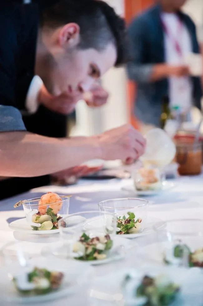 A chef finishing prawn and salad starters in glass bowls at an event
