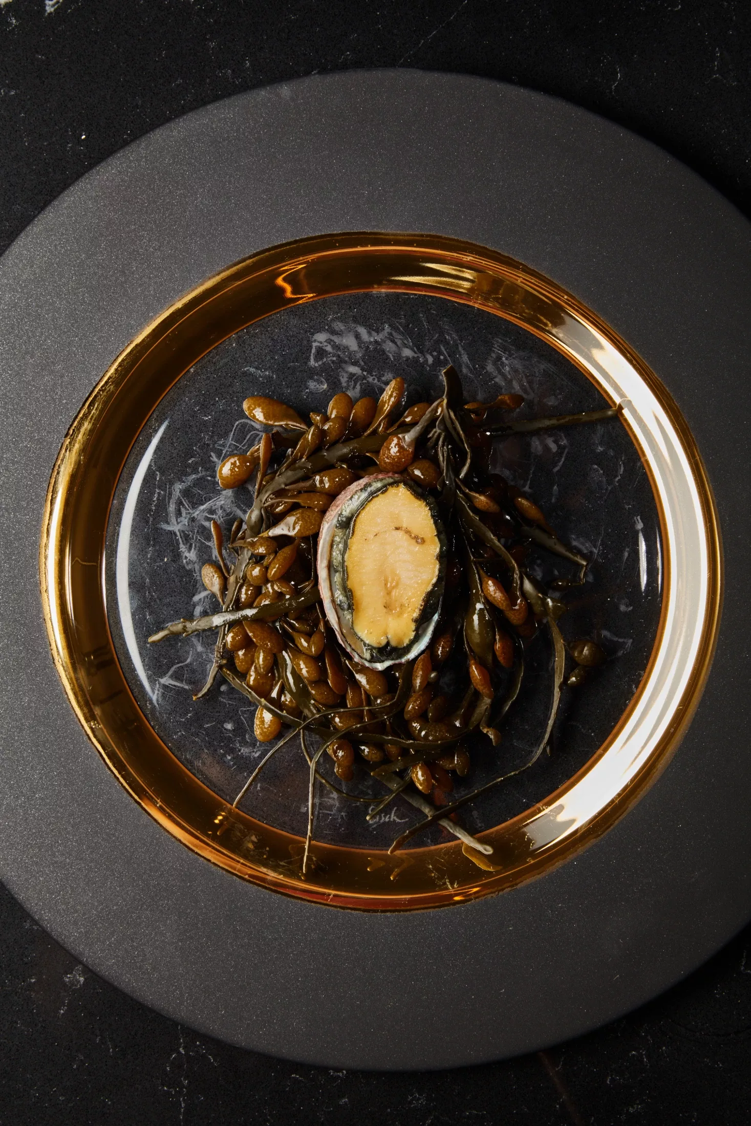 Braised abalone in its shell, plated in a gold-rimmed bowl