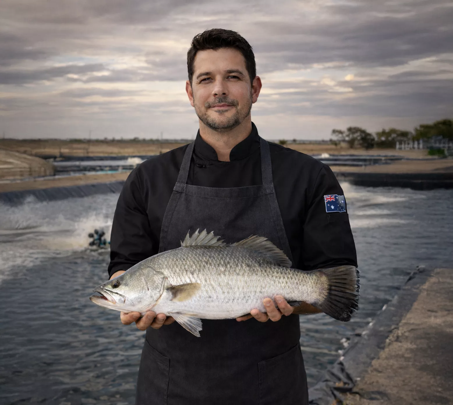 Australian farmer holding a whole farmed barramundi beside the ponds