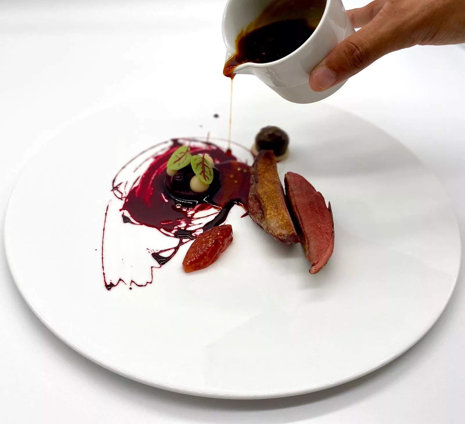A chef pouring jus over a breast of pigeon de Racan in a restaurant kitchen
