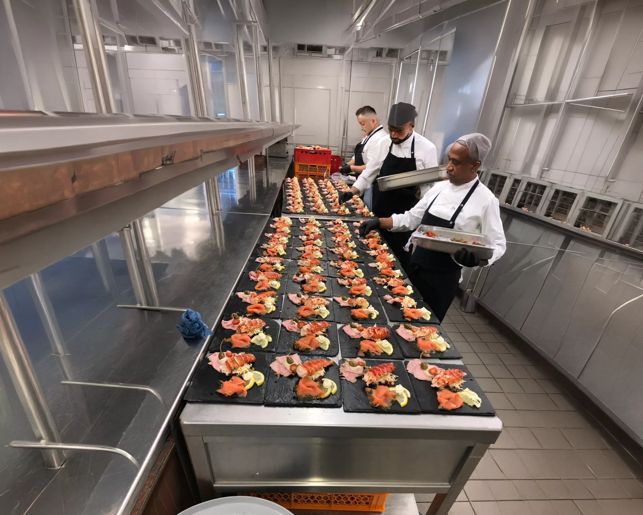 A kitchen brigade plating lobster tail and smoked salmon starters on slate for a banquet